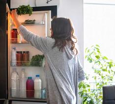 Person åbner et integreret køleskab eller kølefryseskab og overvejer fordele og ulemper